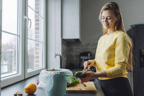 Lächelnde Frau beim Schälen von Zucchini in der Küche zu Hause - OLRF00152