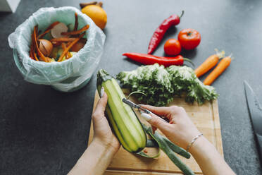 Hands of woman peeling zucchini on kitchen counter at home - OLRF00154