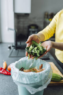 Junge Frau, die Zucchinischalen in die Mülltonne zu Hause wirft - OLRF00156