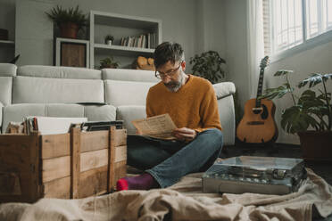 Mann liest Zeitung und sitzt zu Hause neben einem Plattenspieler - DMGF01215