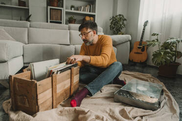 Mann sucht Schallplatten in einer Holzkiste, die mit einem Plattenspieler im Wohnzimmer steht - DMGF01216