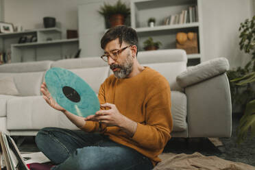 Mann sieht sich eine altmodische Schallplatte an, die im Wohnzimmer steht - DMGF01221