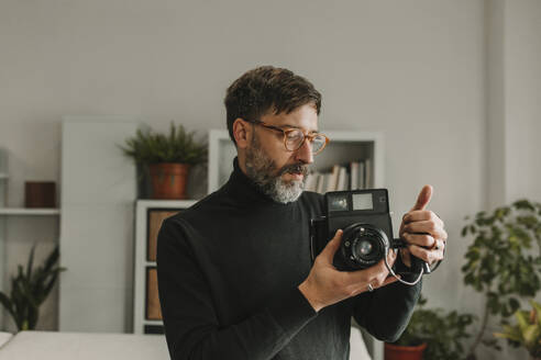 Man holding retro instant camera standing at home - DMGF01246