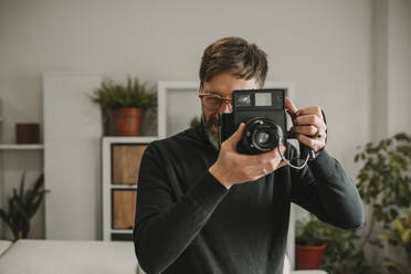 Man photographing through old instant camera at home - DMGF01247