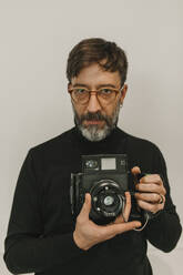 Mann mit altmodischer Sofortbildkamera vor weißem Hintergrund - DMGF01249