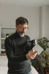 Man with old instant camera and photograph standing at home - DMGF01251