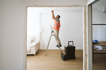 Handwerker steht auf einer Leiter und arbeitet in einem Haus, das gerade renoviert wird - EBBF08619