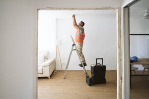 Handwerker steht auf einer Leiter und arbeitet in einem Haus, das gerade renoviert wird - EBBF08619
