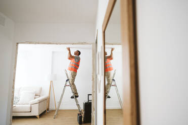 Handwerker, der auf einer Leiter steht und die Decke seines Hauses untersucht - EBBF08620