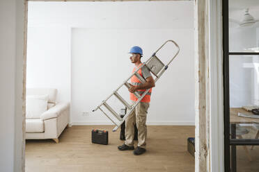 Maintenance engineer carrying ladder in house under renovation - EBBF08626