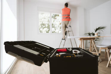 Geöffneter Werkzeugkasten mit einem Handwerker im Hintergrund, der zu Hause arbeitet - EBBF08627