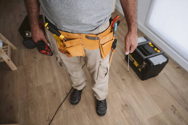 Repairman wearing tool belt and standing at home - EBBF08632