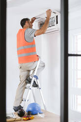Älterer Techniker steht auf einer Leiter und prüft eine Klimaanlage zu Hause - EBBF08636