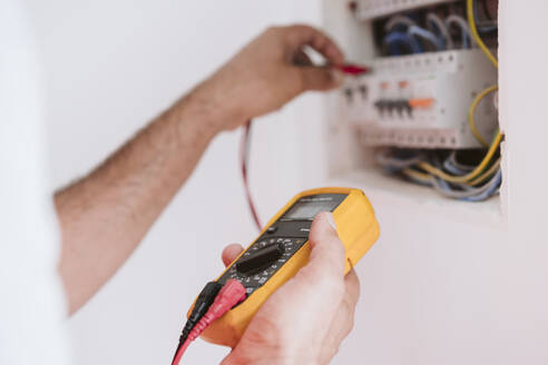 Mature technician measuring voltage near fuse box at home - EBBF08643
