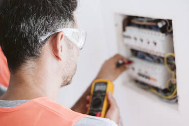 Electrician measuring voltage near fuse box at home - EBBF08644