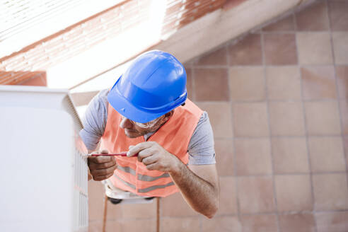 Techniker mit blauem Schutzhelm bei der Reparatur einer Klimaanlage in einem Haus, das gerade renoviert wird - EBBF08649