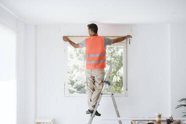 Älterer Handwerker misst Fenster in einem zu renovierenden Haus - EBBF08662
