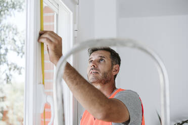 Maintenance engineer measuring window length at house under renovation - EBBF08664