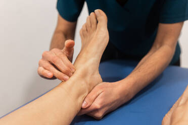 Ein Physiotherapeut beurteilt den Fuß eines Patienten, indem er auf einem klinischen Untersuchungstisch nach Problemen tastet - ADSF52838