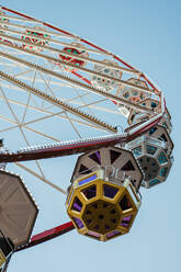 From below close-up of a vibrant Ferris wheel's cabins and intricate metalwork against a clear sky - ADSF52842