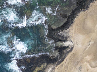 Luftaufnahme der schäumenden Wellen, die gegen die felsige Küste und den Sandstrand an der Nordküste Fuerteventuras bei Faro del Toston schlagen - ADSF52856