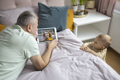 Großvater und Baby Videoanrufe einer jungen Frau von einem Tablet in einem gemütlichen Schlafzimmer - ADSF52868