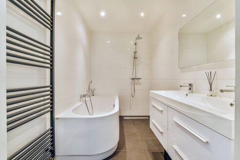Ein makellos gestaltetes, modernes Badezimmer mit einer weißen, freistehenden Badewanne, einem geräumigen Waschtisch mit Schubladen, einem an der Wand befestigten Spiegel und stilvollen Fliesenböden. - ADSF52894