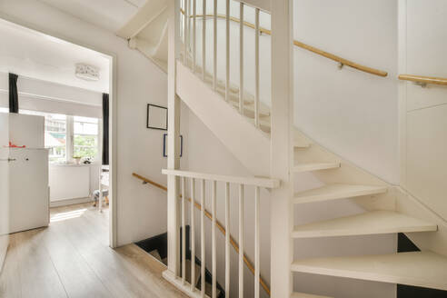 Interior view of a modern home staircase with white steps and wooden handrails against a bright window. - ADSF52903