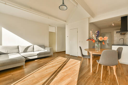 Ein gemütliches und stilvolles Wohnzimmer mit einem großen grauen Sofa, Holzfußböden und einem lichtdurchfluteten Essbereich. - ADSF52905
