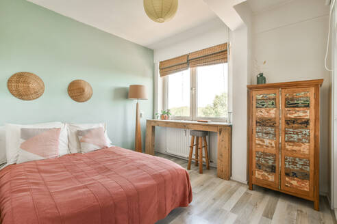 Ein gemütliches, minimalistisches Schlafzimmer mit weißem und aquamarinfarbenem Farbschema, einem bequemen Bett mit korallenroter Bettwäsche und schlichter Wanddekoration aus Korbgeflecht. - ADSF52908
