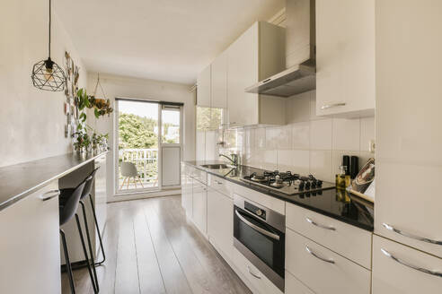 A sleek modern kitchen interior featuring white cabinetry, stainless steel appliances, and a balcony entrance with abundant natural light. - ADSF52915