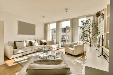 Ein geräumiges, sonnendurchflutetes Wohnzimmer mit einem bequemen beigen Sofa, Sesseln, einem Couchtisch aus Glas und stilvollen Dekorationen. - ADSF52918