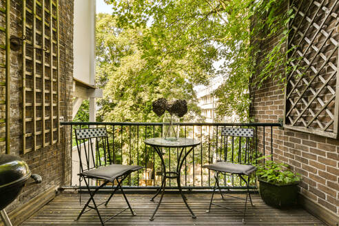 Ein kleiner, einladender Wohnungsbalkon mit einem Bistrotisch und Stühlen, Topfpflanzen und üppigem Grün im Hintergrund bietet einen ruhigen urbanen Rückzugsort. - ADSF52921