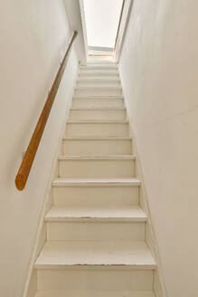 A simple white staircase with a wooden handrail extends upwards, leading to a bright skylight. - ADSF52922