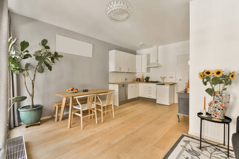 Eine helle, moderne Küche mit weißen Schränken, einem Esstisch aus Holz und dekorativen Pflanzen, die die einladende Atmosphäre unterstreichen. - ADSF52926