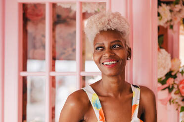 Positive panamanian woman with curly hair smiling and looking at camera while standing in floral shop - ADSF52941