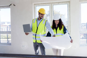 Smiling architect discussing over blueprint with colleague at site - AAZF01504