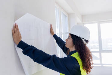 Architect examining blueprint on wall at site - AAZF01505