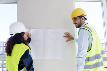Architects discussing over blueprint on wall at site - AAZF01507
