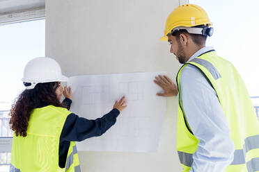 Architect explaining blueprint to colleague at site - AAZF01508