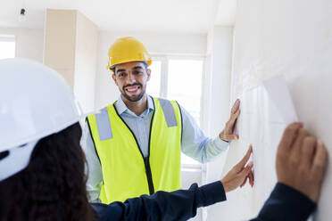 Smiling architect listening to colleague explaining blueprint at site - AAZF01510