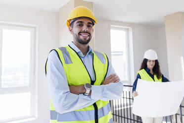 Smiling confident architect with colleague in background at site - AAZF01520