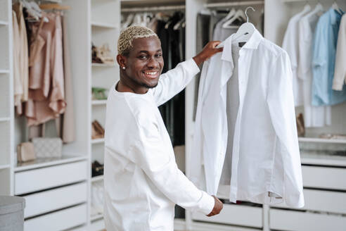 Glücklicher Mann mit weißem Hemd vor einem Kleiderschrank - NLAF00306