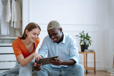 Glücklicher junger Mann und Frau, die zu Hause einen Tablet-PC benutzen - NLAF00330