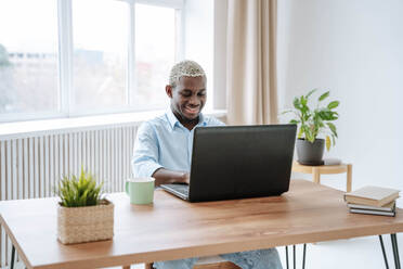 Smiling freelancer working on laptop at desk in home office - NLAF00352