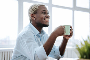 Happy man holding coffee cup at home - NLAF00354