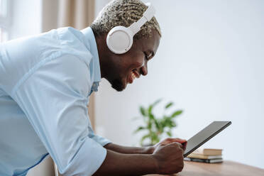 Glücklicher Mann mit drahtlosen Kopfhörern und Tablet-PC - NLAF00356