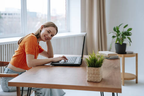 Lächelnder junger Freiberufler mit Laptop sitzend - NLAF00357