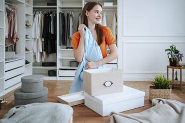 Smiling young woman folding clothes near boxes - NLAF00363