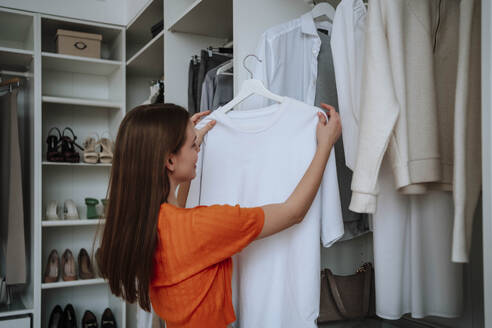 Frau hält weißes T-Shirt in der Nähe des Kleiderschranks - NLAF00369